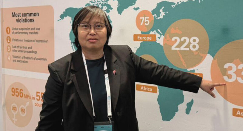 Woman in a black blazer points at a world map infographic during a presentation or conference.